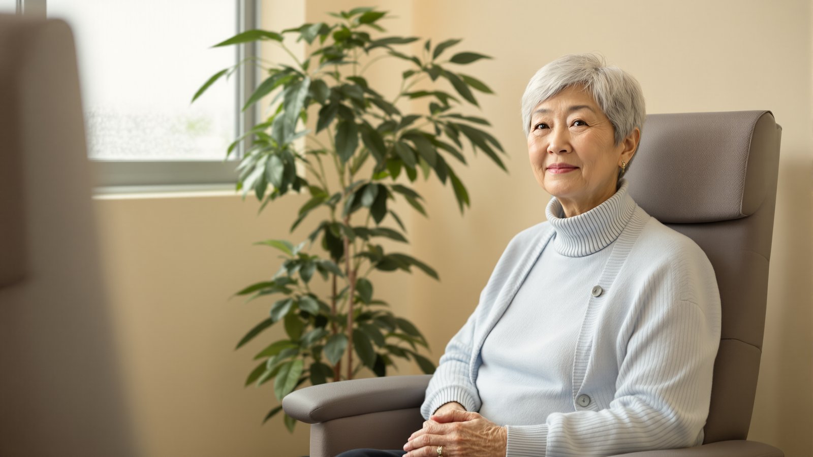 An older Korean American woman waiting calmly in a clinic exam room with hands folded in her lap.