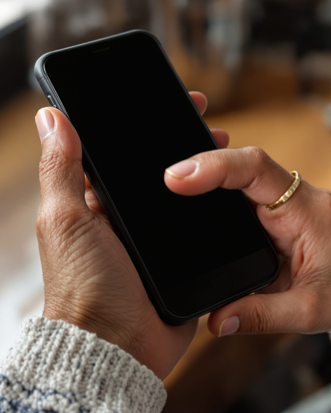 A senior's hand holding an iPhone with a pure black screen.
