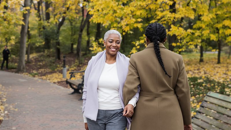 A mother and adult daughter walking together along a garden path — when to start the assisted-living conversation.