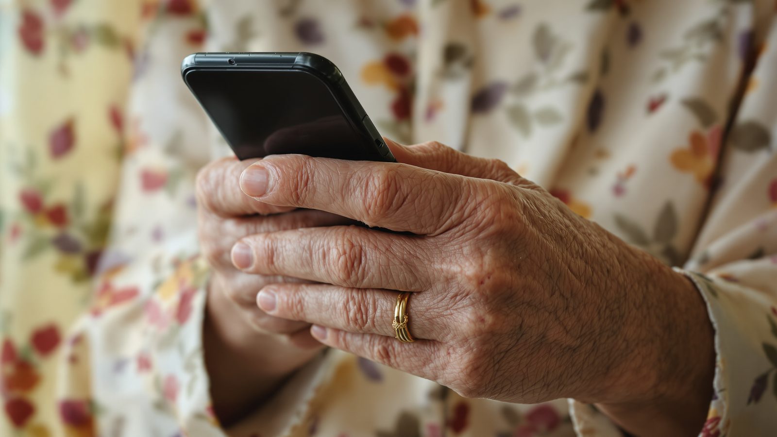 An older woman's hands holding an iPhone with an unlit screen — text message scams targeting seniors.